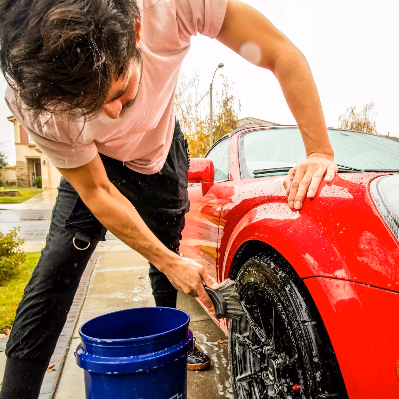 man cleaning red car on a rainy day