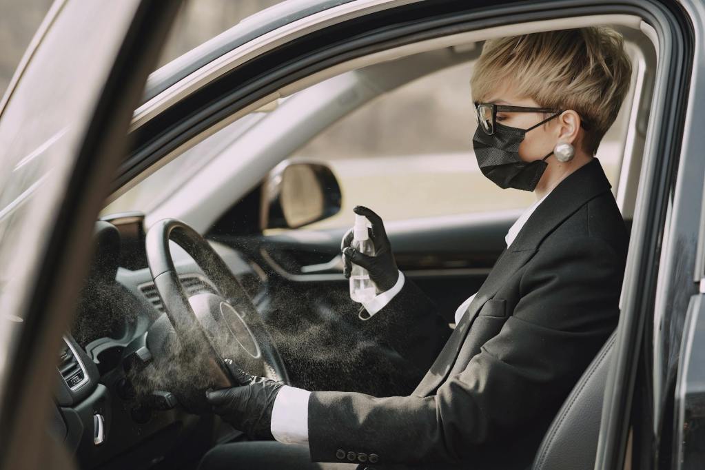 woman in formal clothes disinfecting steering wheel of car