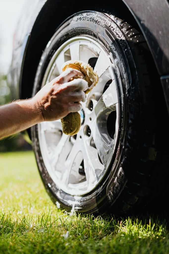 person holding sponge washing car tire
