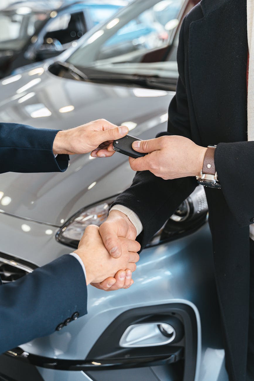 close up of men shaking hands and handing in keys to a new car at the car salon