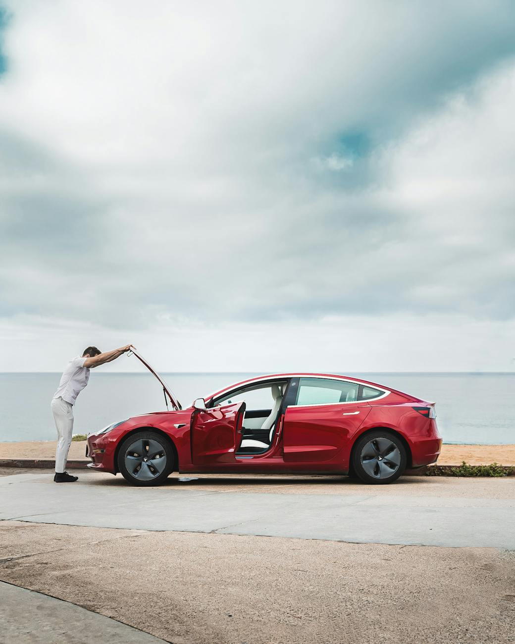 man repairing red car by the sea